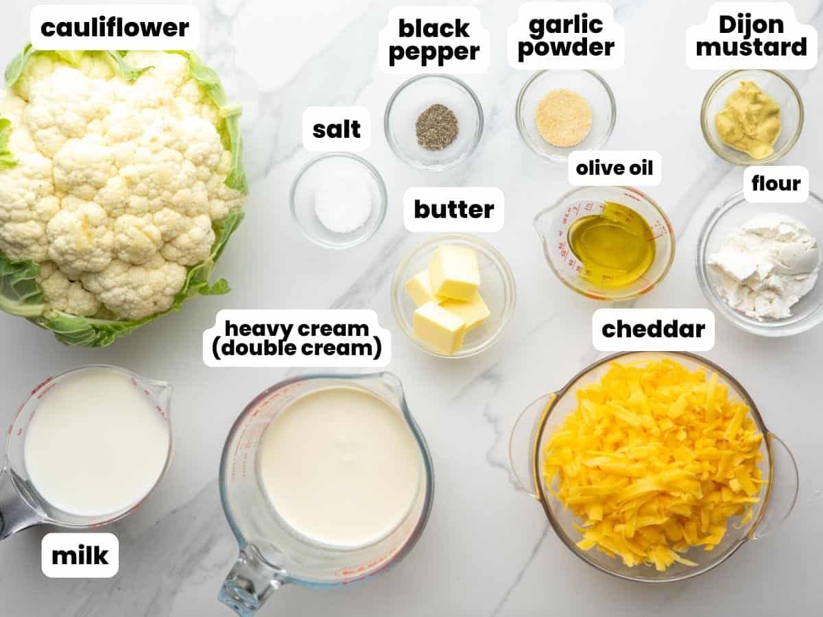 Ingredients needed to make cauliflower mac and cheese, including cheddar cheese, butter, cream, and a whole head of cauliflower.