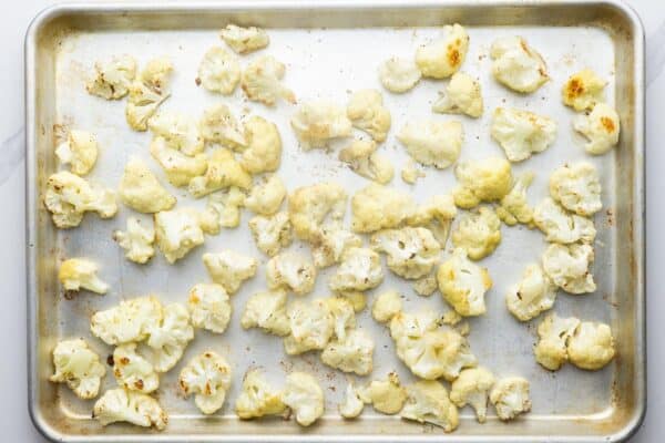 lightly roasted cauliflower florets for cauliflower cheese on a metal sheet pan.