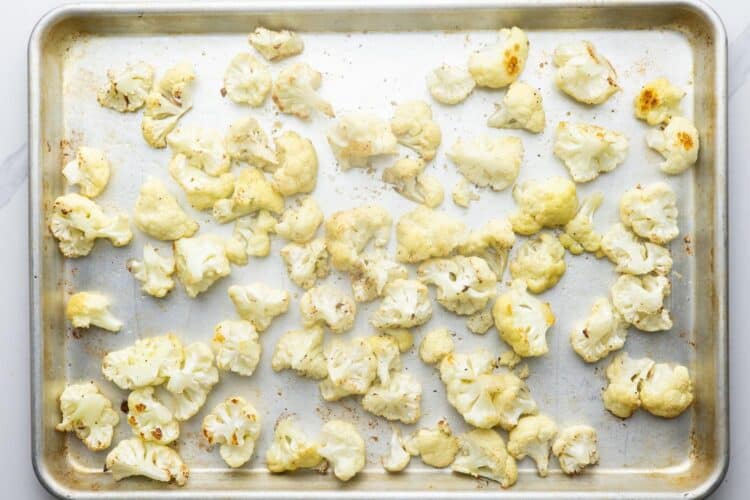 lightly roasted cauliflower florets for cauliflower cheese on a metal sheet pan.