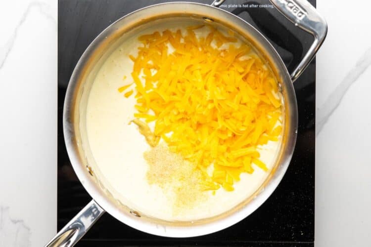 seasonings and shredded cheddar cheese added to a cream sauce to create the cheese sauce for cauliflower mac and cheese.