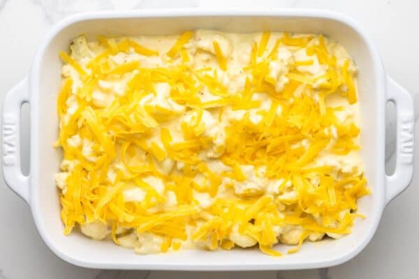shredded cheddar cheese added to a pan of cheesy cauliflower.