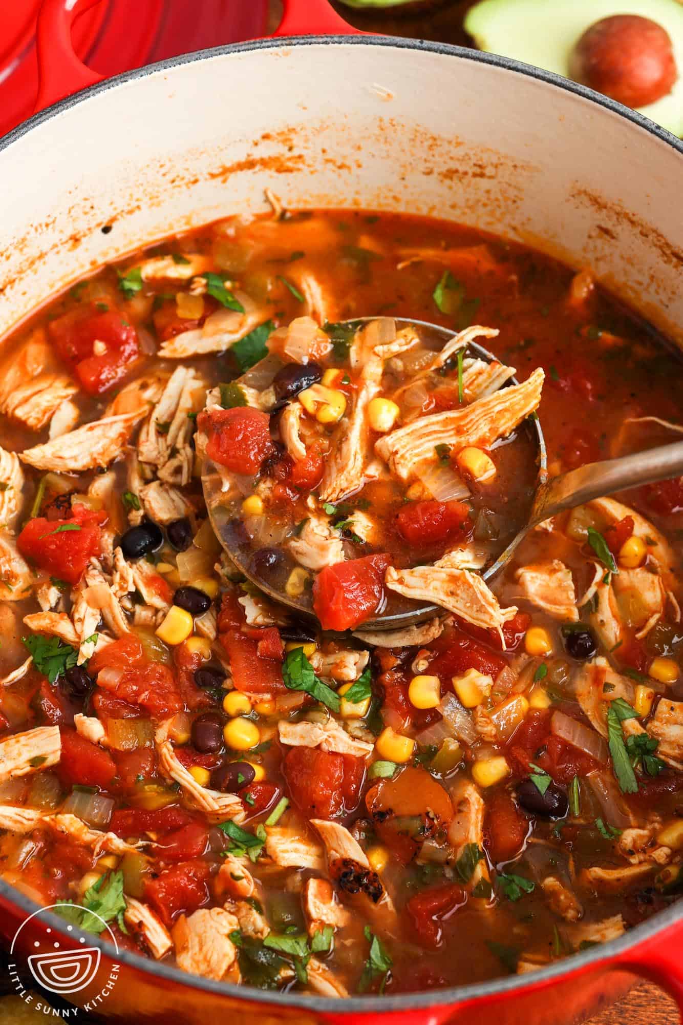a red dutch oven filled with chicken tortilla soup, with tomatoes, corn, and black beans.