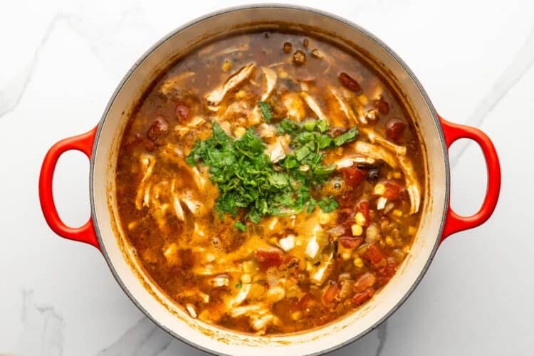 a dutch oven of chicken tortilla soup. Chopped cilantro is added at the end.