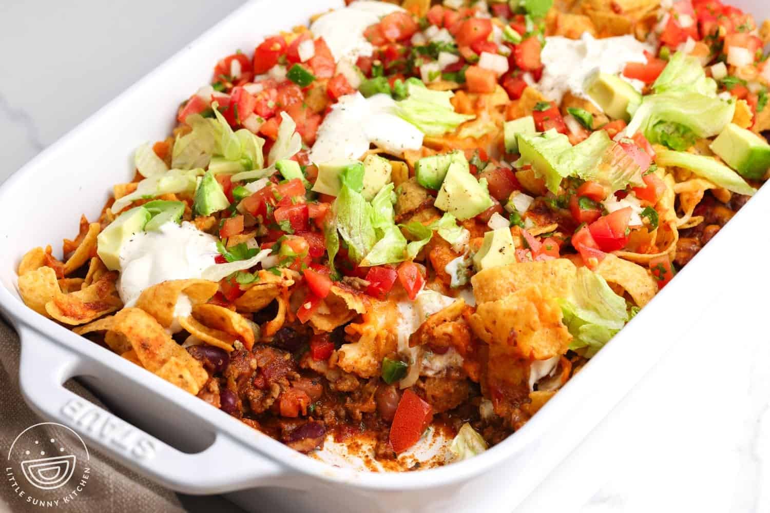 closeup of a frito pie casserole with layers of beef, beans, chips, cheese, and fresh toppings, including sour cream and avocado.