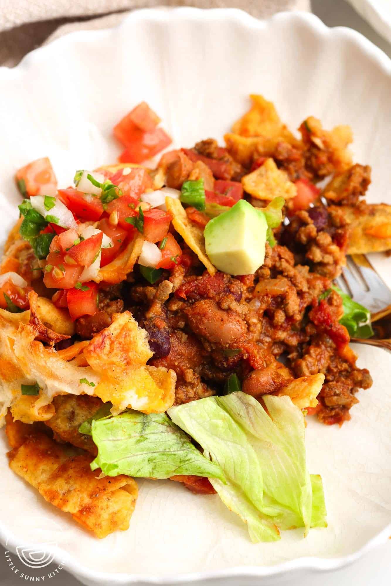 a serving of frito pie in a white fluted bowl.