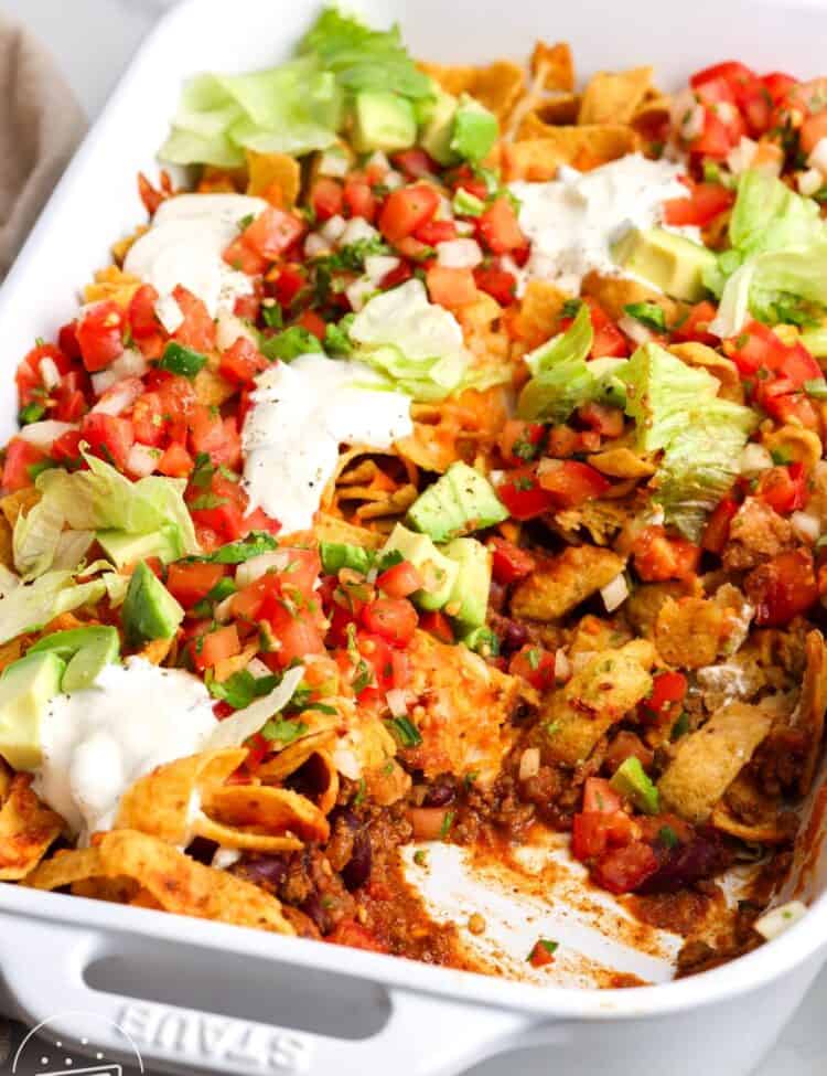 closeup of a frito pie casserole with layers of beef, beans, chips, cheese, and fresh toppings, including sour cream and avocado.