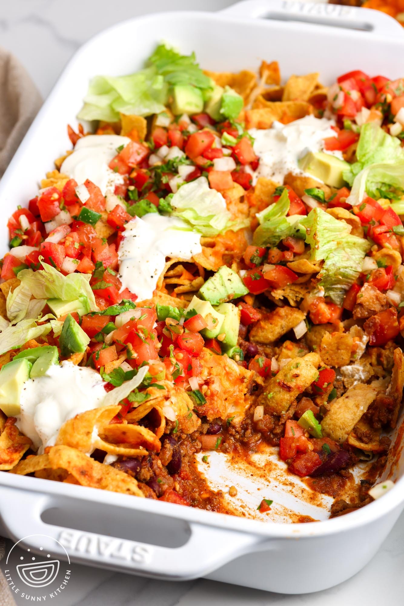 closeup of a frito pie casserole with layers of beef, beans, chips, cheese, and fresh toppings, including sour cream and avocado.
