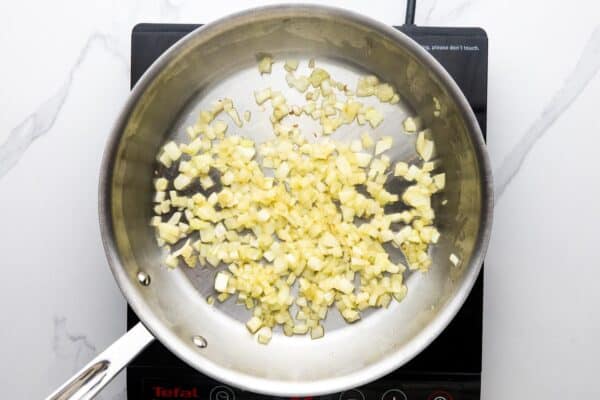 diced onion sauteing in a stainless steel skillet over an electric burner.