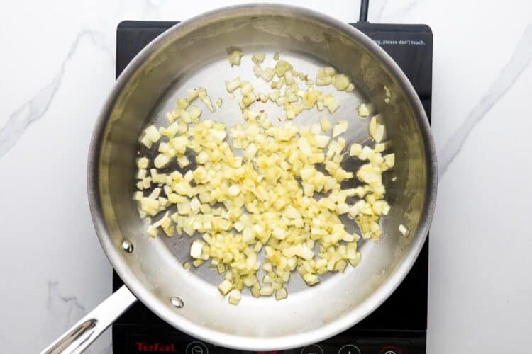 diced onion sauteing in a stainless steel skillet over an electric burner.