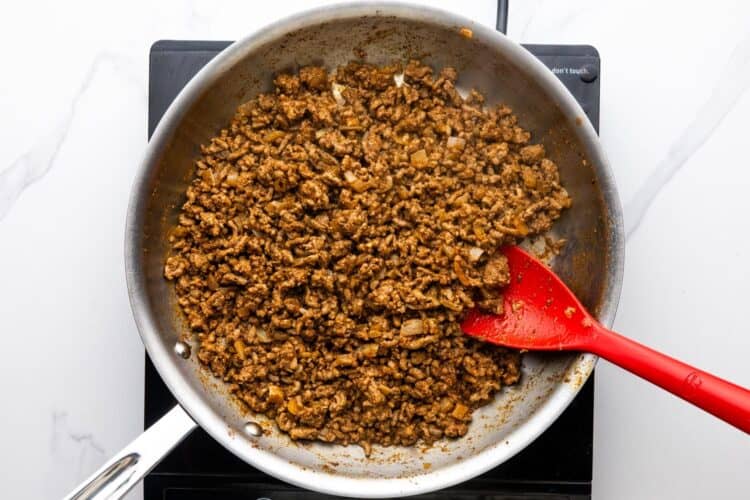 seasoned ground beef taco meat cooking in a skillet, stirred with a red spatula.