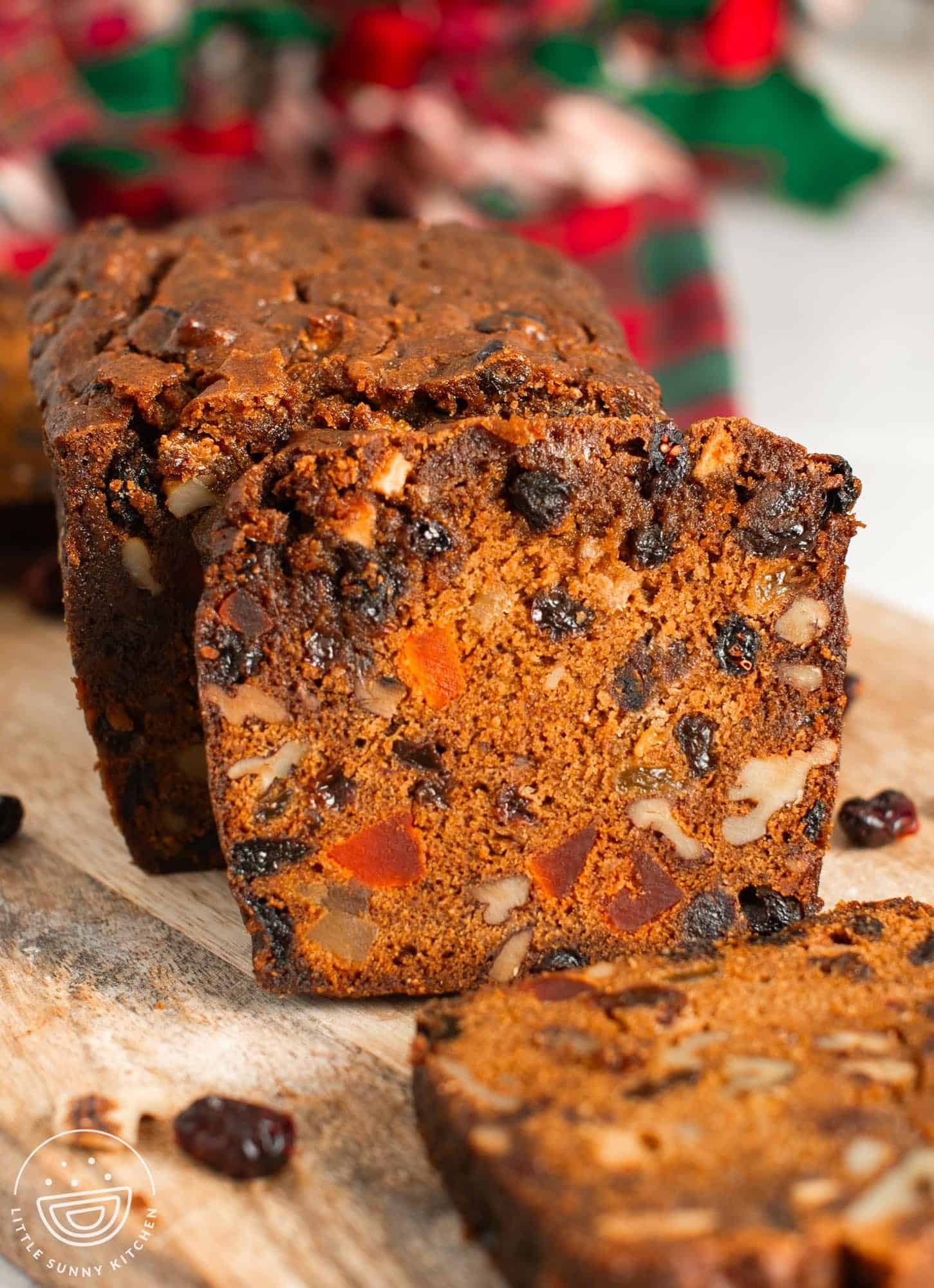 A sliced loaf of fruit cake on a wooden cutting board.