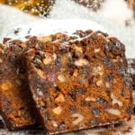 Two slices of fruit cake leaned against the loaf. Inside each slice is plenty of dried fruit and walnuts. Powdered sugar is dusting over the bread.