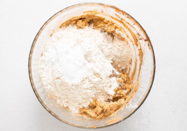 dry ingredients added to butter mixture for fruitcake batter in a large glass mixing bowl.