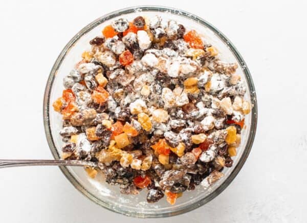 soaked fruits and nuts dusted with flour, added to fruit cake batter in a large glass bowl.