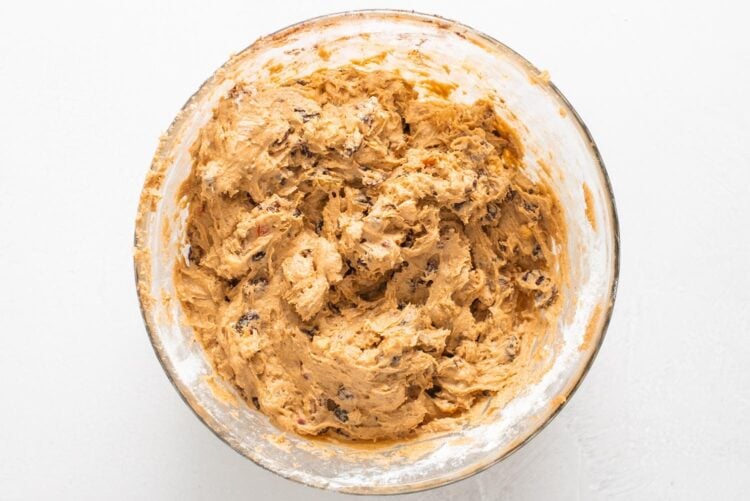 thick fruitcake batter with dried fruits and nuts in a large glass mixing bowl.