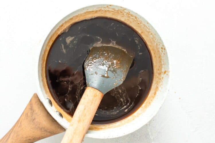 fruit cake syrup made with brandy and brown sugar, cooking in a small saucepan, stirred with a spatula.