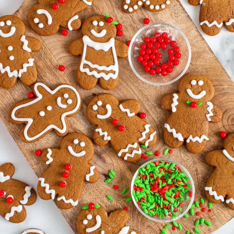 a dozen decorated gingerbread men cookies arranged on a wooden cutting board.