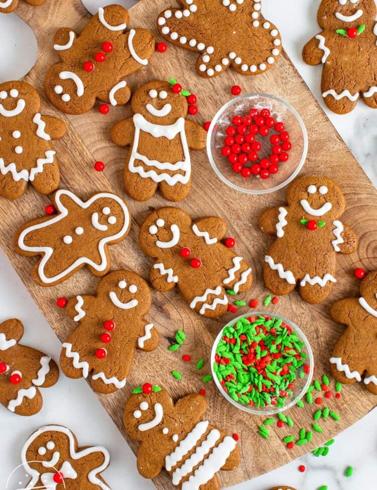 a dozen decorated gingerbread men cookies arranged on a wooden cutting board.