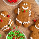 large gingerbread man cookies arranged on a wooden board along with small clear bowls of holiday sprinkles. The cookies are decorated in the traditional way with white icing.