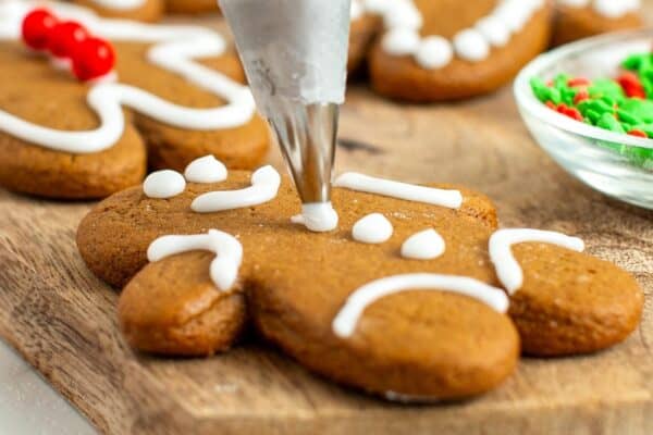 closeup of the process of adding icing details to baked gingerbread cookies with a piping bag.