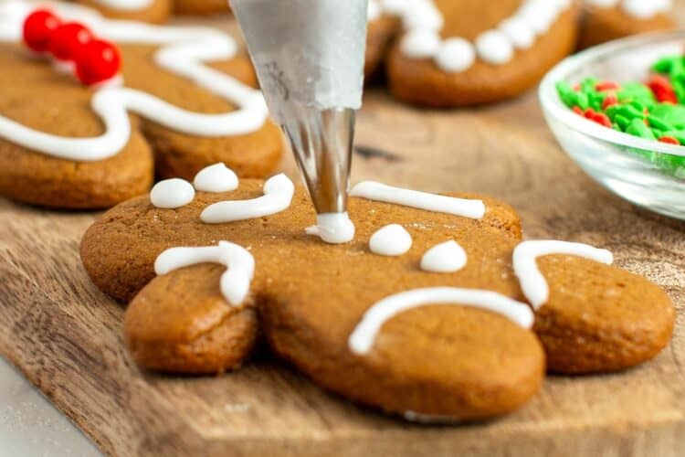 closeup of the process of adding icing details to baked gingerbread cookies with a piping bag.