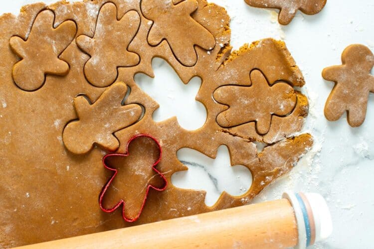 gingerbread cookie dough rolled out on a marble surface with flour. A red cookie cutter is making gingerbread men.