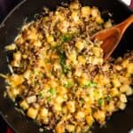 a large frying pan of ground beef and potatoes topped with cheese, on the table, being served.