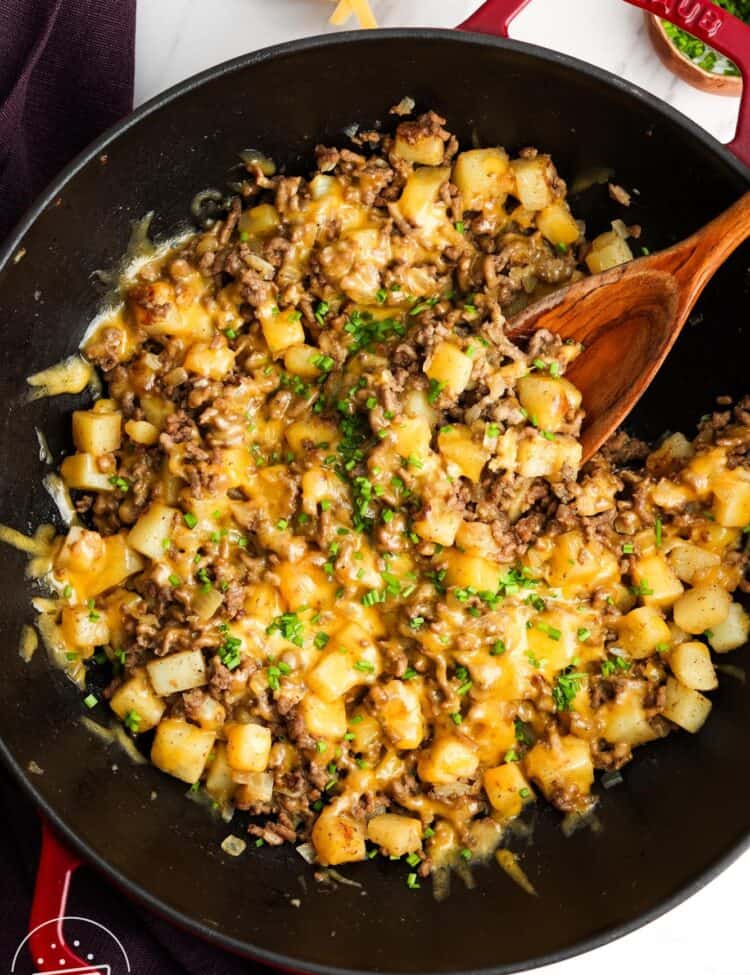 a large frying pan of ground beef and potatoes topped with cheese, on the table, being served.