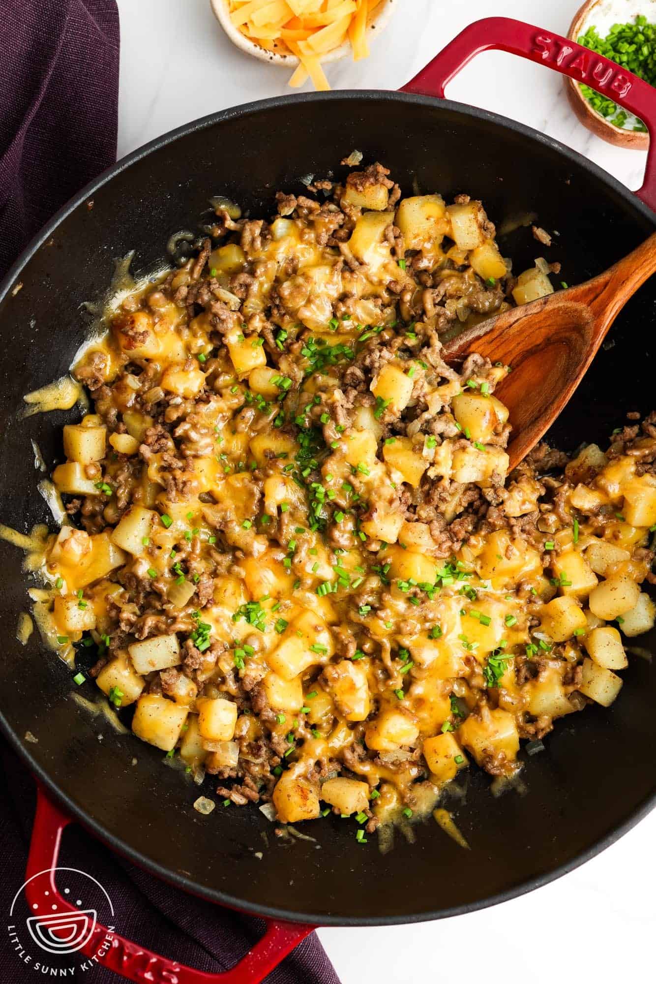 a large frying pan of ground beef and potatoes topped with cheese, on the table, being served.