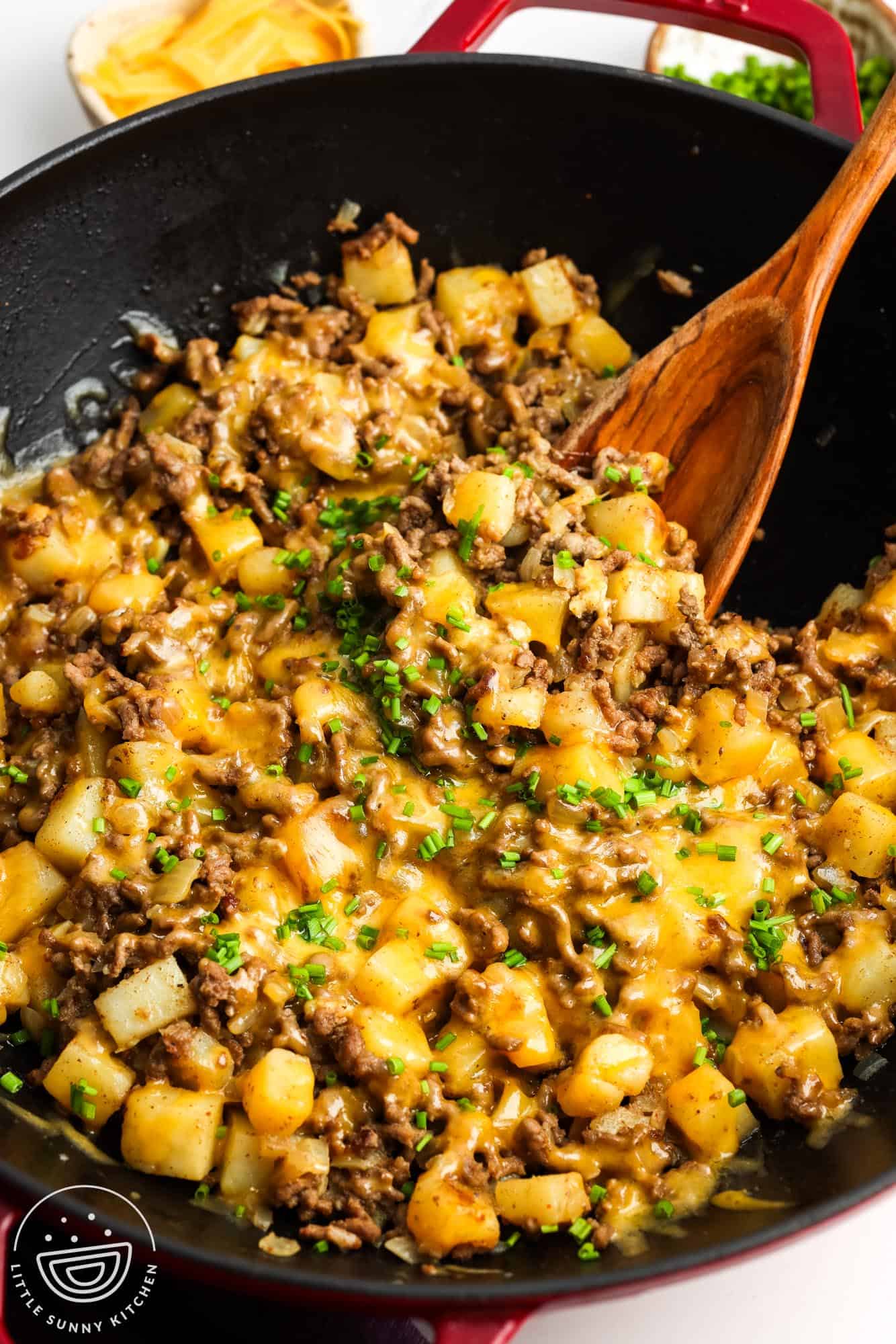a large black skillet filled with cheesy ground beef and potatoes, served with a large wooden spoon.