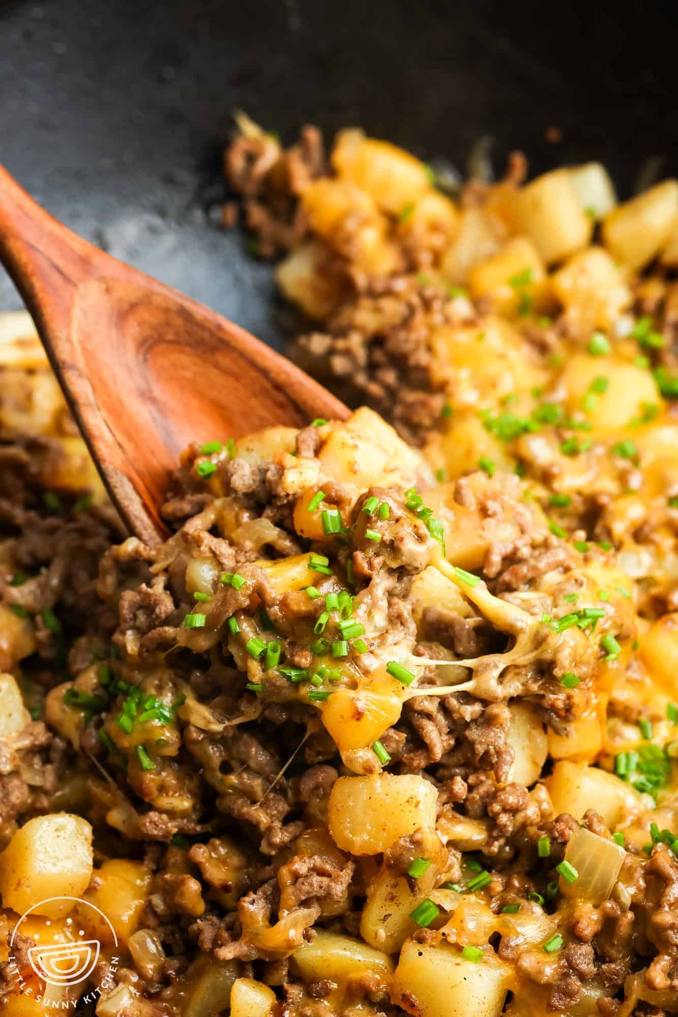 closeup of ground beef and potatoes recipe. a spoon is serving it, showing melty cheese and tender cubed potatoes.