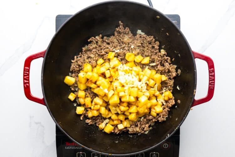 minced garlic and potatoes added to cooked ground beef in a frying pan.