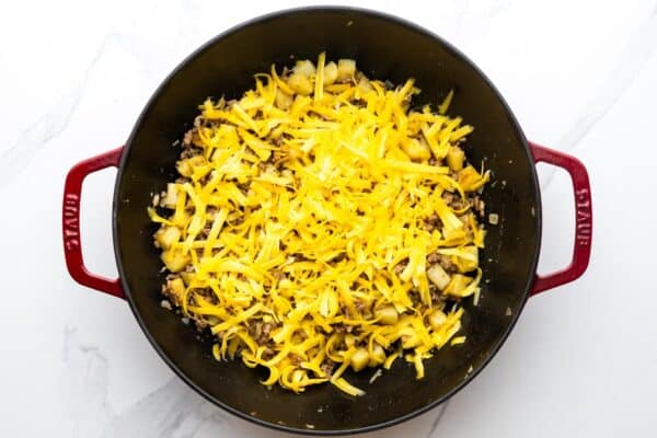 shredded cheese added to a skillet of ground beef and potatoes.