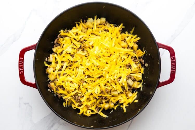 shredded cheese added to a skillet of ground beef and potatoes.