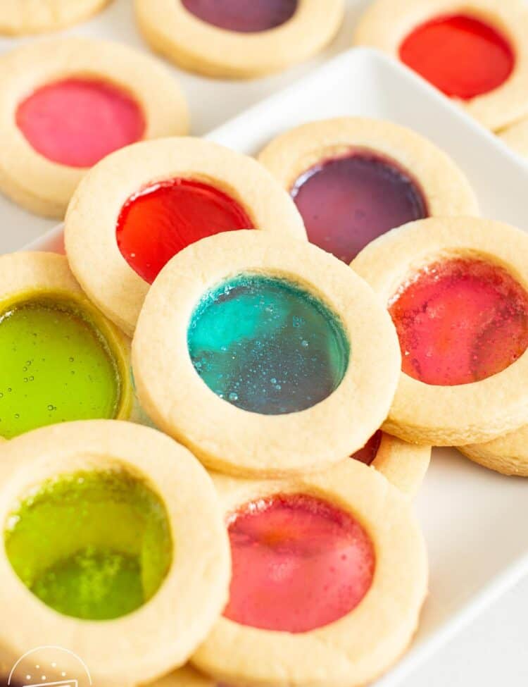 closeup of a rectangular plate holding round cutout cookies with candy windows in the center.