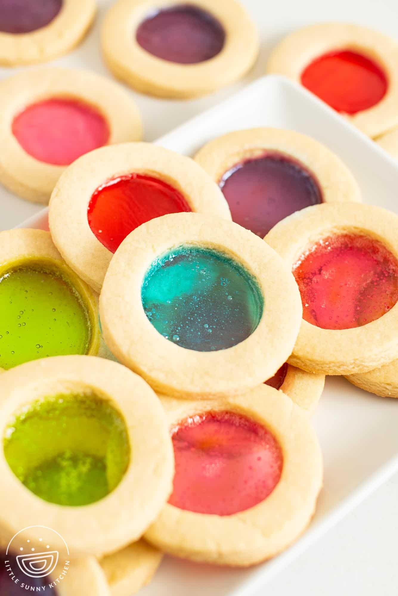 closeup of a rectangular plate holding round cutout cookies with candy windows in the center.