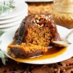 small sticky toffee pudding on a white plate with toffee sauce and chopped pecans.