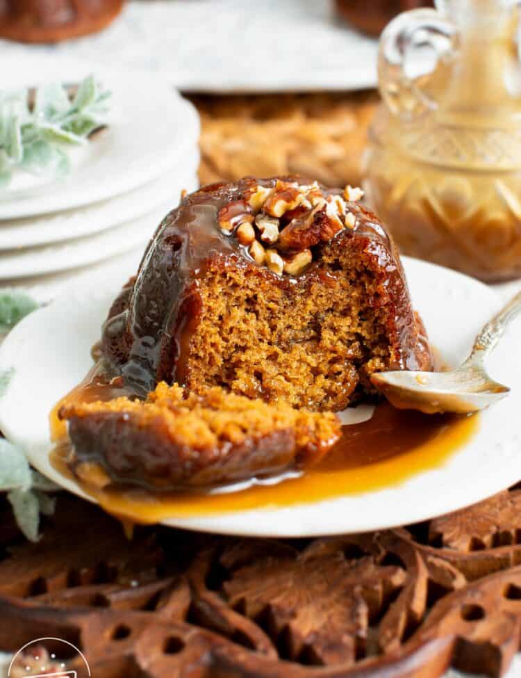 small sticky toffee pudding on a white plate with toffee sauce and chopped pecans.