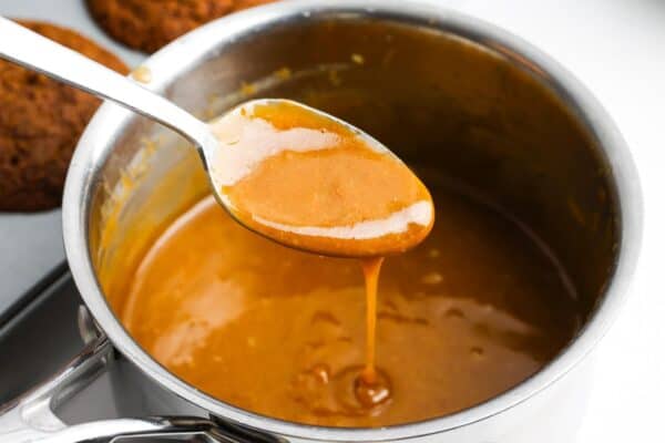 toffee sauce cooking in a saucepan, a spoon is holding it up.