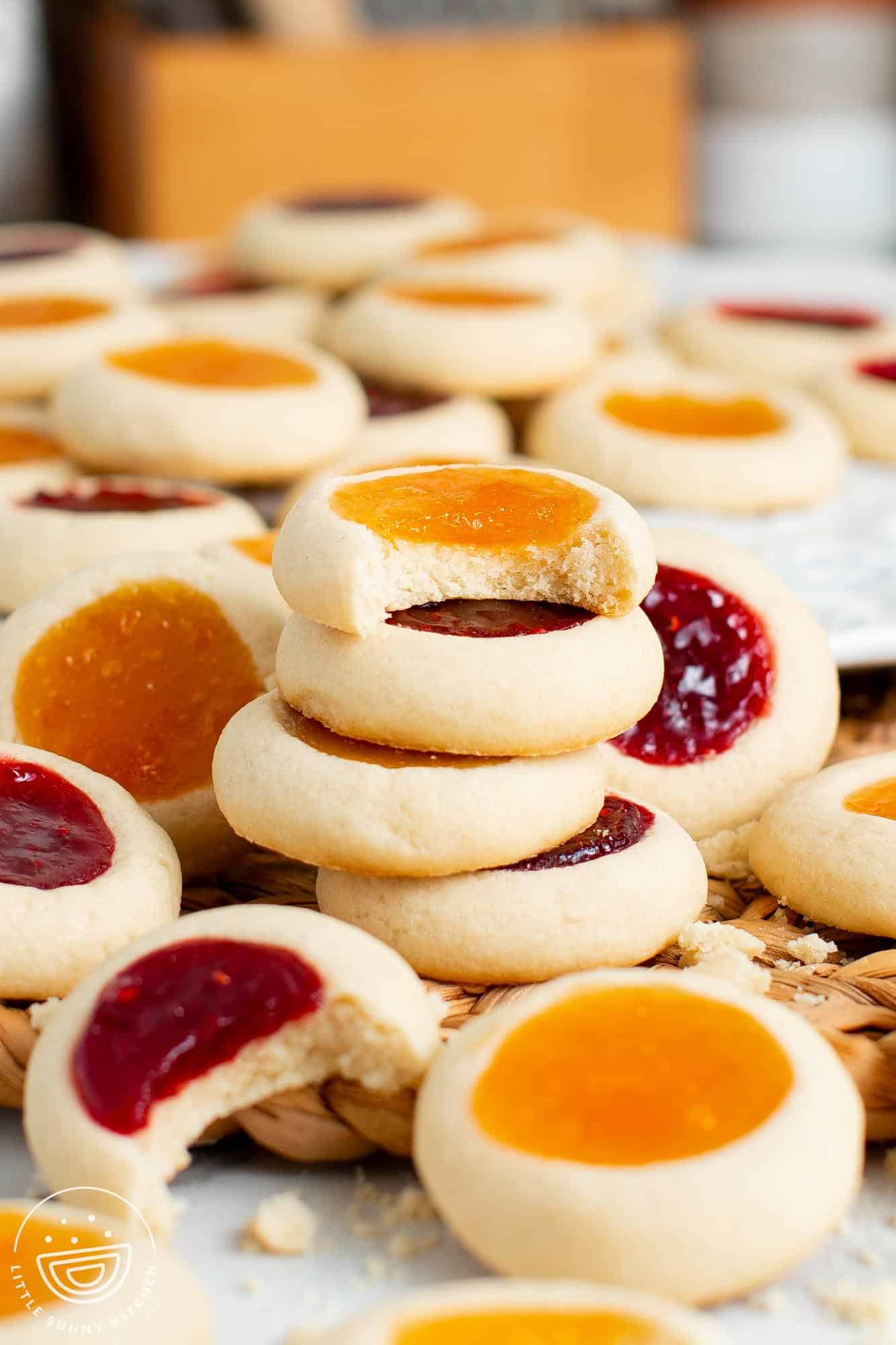 a stack of thumbprint cookies among many other of the same cookies. The top cookie on the stack of four has had a bite taken from it.