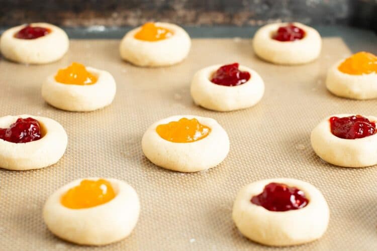 unbaked thumbprint cookies, some filled with yellow apricot jam, others with red raspberry jam.