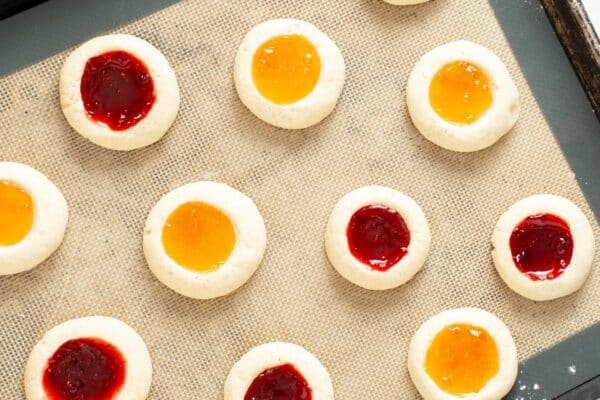 overhead view of a pan of baked thumbprint cookies with apricot and raspberry jam filling.