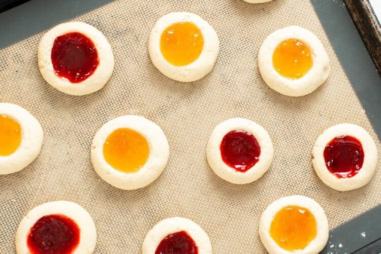 overhead view of a pan of baked thumbprint cookies with apricot and raspberry jam filling.
