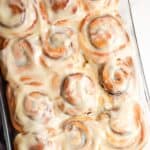 12 cinnamon rolls with icing in a glass 9x13-inch baking pan, set on a marble counter.