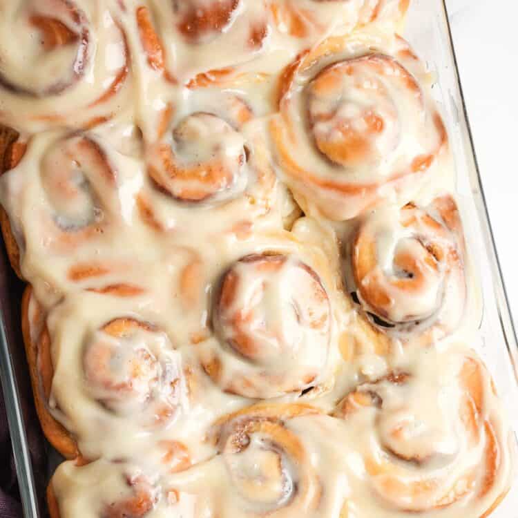 12 cinnamon rolls with icing in a glass 9x13-inch baking pan, set on a marble counter.