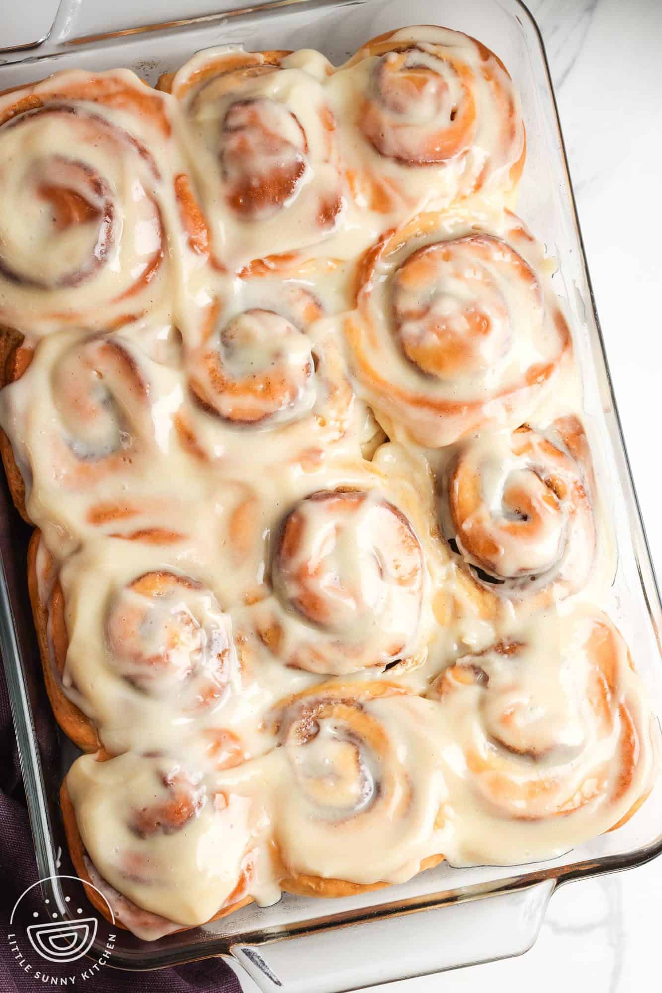 12 cinnamon rolls with icing in a glass 9x13-inch baking pan, set on a marble counter.