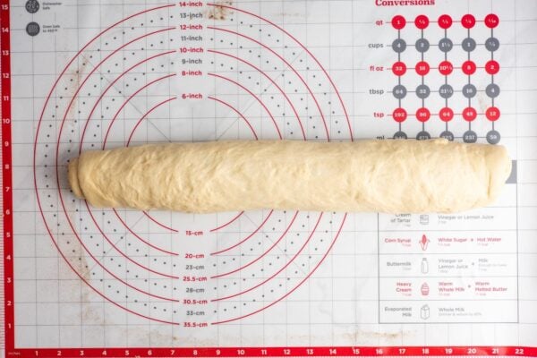 cinnamon roll dough rolled into a log on a baking mat that shows conversions and measurements.