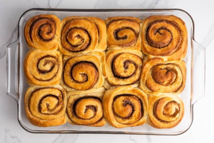 baked cinnamon rolls without icing in a glass baking pan, set on a marble counter.