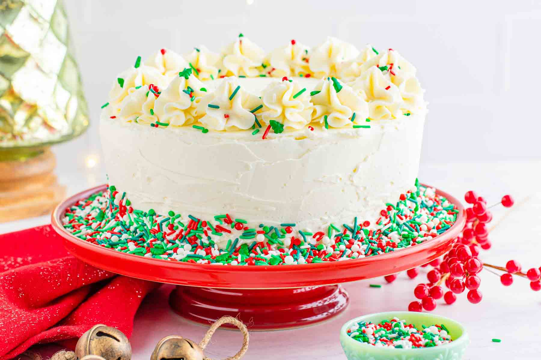 Christmas funfetti cake frosted with vanilla buttercream and decorated with red green and white sprinkles on a red cake stand