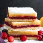 three layered lemon cranberry bars, stacked on a small white plate, garnished with fresh cranberries.